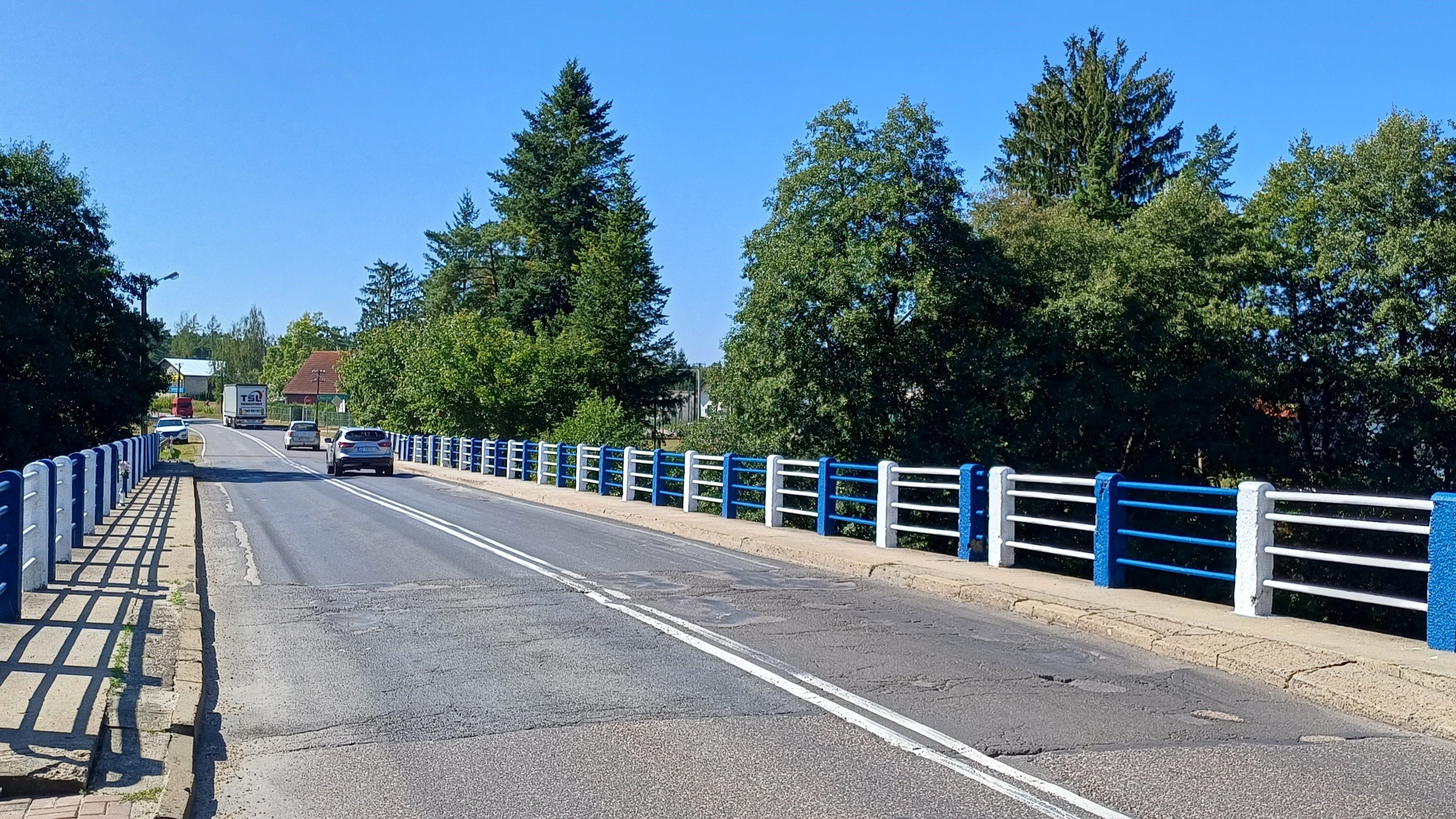 Zdjęcie przedstawia most nad Brdą w ciągu drogi wojewódzkiej nr 235 w Męcikale przed remontem. Po bokach obiektu stare, betonowe słupki ze stalowymi barierami. Stara nawierzchnia mostu Po moście, w oddali jadą samochody.