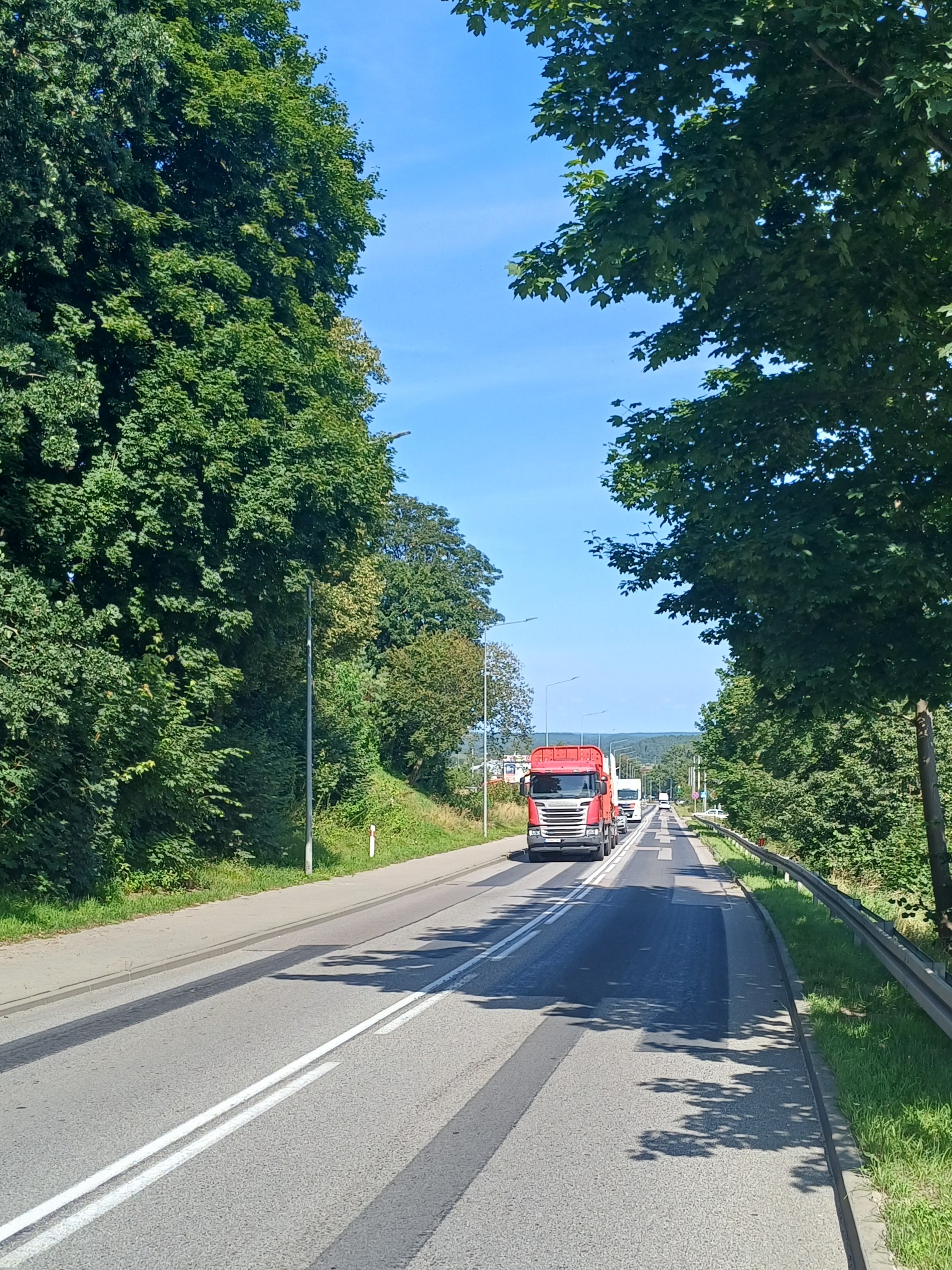 Droga wojewódzka nr 212 w Bytowie. Drogą, która nosi ślady napraw nawierzchni, jedzie samochód ciężarowy. Po obu stronach drogi drzewa i infrastruktura towarzysząca: chodni, oświetlenie drogowe i bariery ochronne.