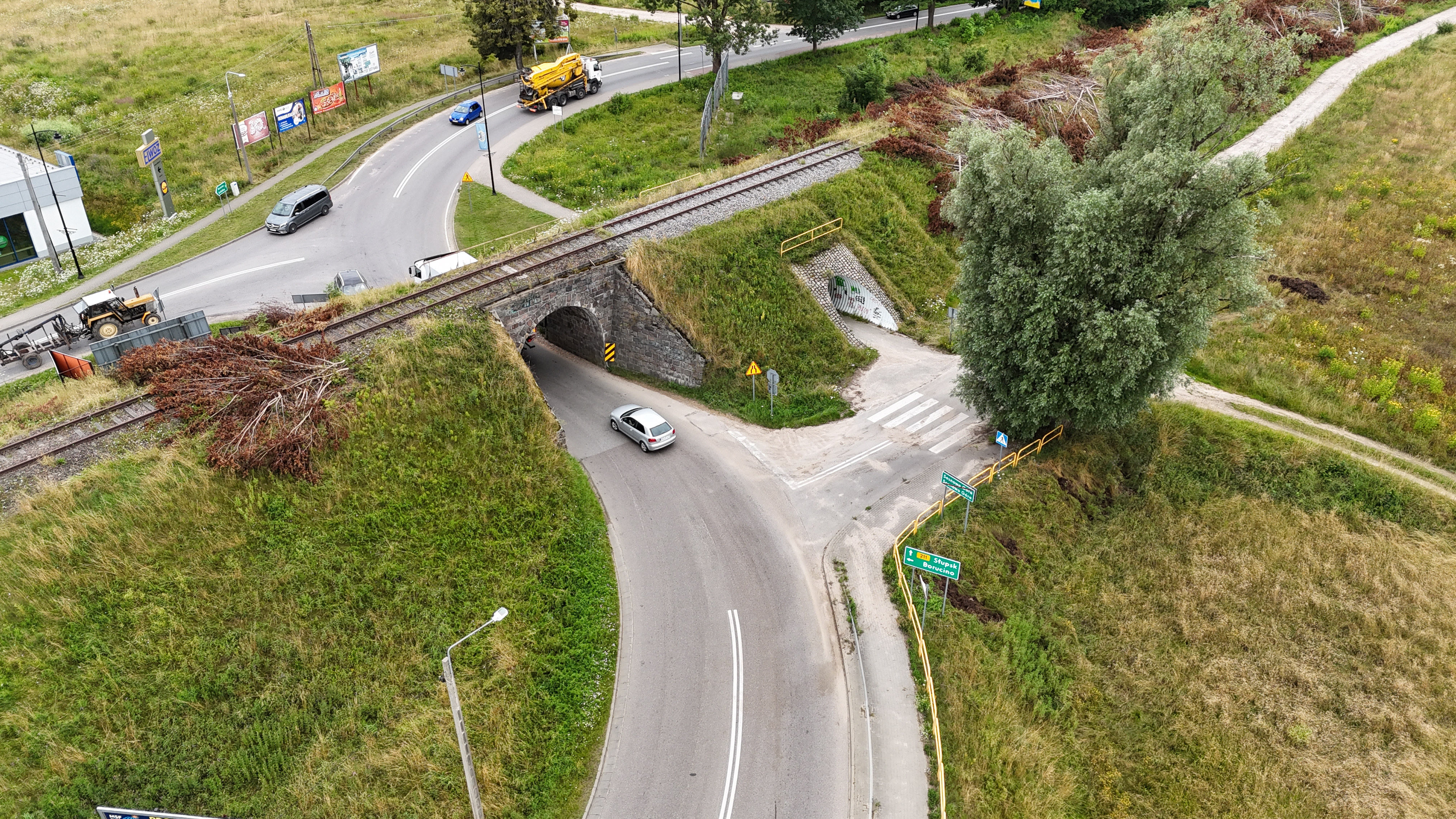 Stan obecny skrzyżowania drogi wojewódzkiej nr 211 z drogą powiatową i gminną oraz linia kolejową nr 229 w Sierakowicach. Na pierwszym planie skrzyżowanie z drogą gminną i nasyp kolejowy z dwoma wiaduktami z linią kolejową. Pod większym wiaduktem jest droga wojewódzka, przy mniejszym chodnik. Drogą poruszają się samochody.